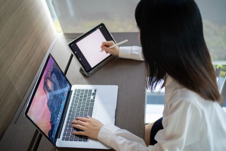 Asian woman multitasking with laptop and tablet in a modern home office in Bangkok.
